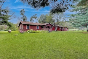 A red house with a porch, surrounded by a well-maintained lawn and trees.