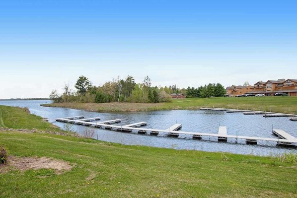 A river with docks, a grassy bank, and a building complex in the background. - Lovely home overlooking golf course with WiFi, AC, pool, hot tub - near lake (Arkdale)