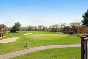 Golfkenttä, jossa on klubitalo, suuri puu ja parvekkeellinen rakennus.