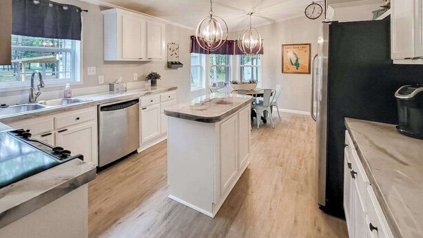 A modern kitchen with white cabinetry, a central island, pendant lighting, and a dining area with a view of the outdoors. - Peaceful 3BR home w/ 3 season clubhouse 1/2 mile from Castle Rock Lake (Mauston)