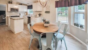 A modern kitchen with white cabinets, a central island, and a dining area with a round table and chairs. - Peaceful 3BR home w/ 3 season clubhouse 1/2 mile from Castle Rock Lake (Mauston)
