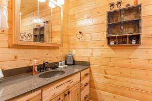 Interior de una cabaña de madera con un espejo grande, un lavabo y una repisa con adornos.
