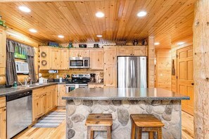 A kitchen with wooden cabinets, a granite countertop, a stone island, and stainless steel appliances.