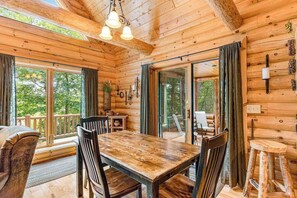 A wooden cabin interior with a dining table, chairs, and a large window.