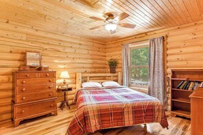Una habitación de cabaña de madera con cama, cómoda, lámpara y estantería.