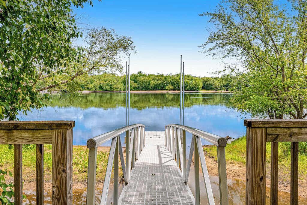 A wooden dock leading to a calm lake surrounded by greenery.