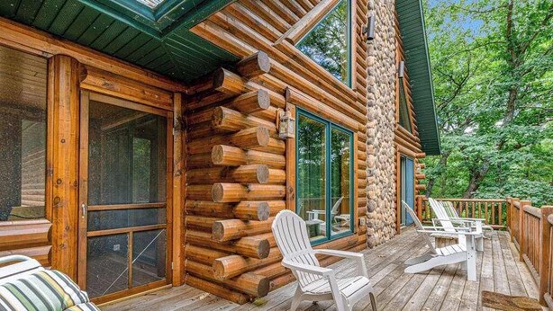 Una cabaña de troncos con terraza, sillas Adirondack y un sofá.
