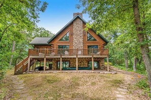 A log cabin with a stone chimney, a balcony, and a staircase leading to the entrance.