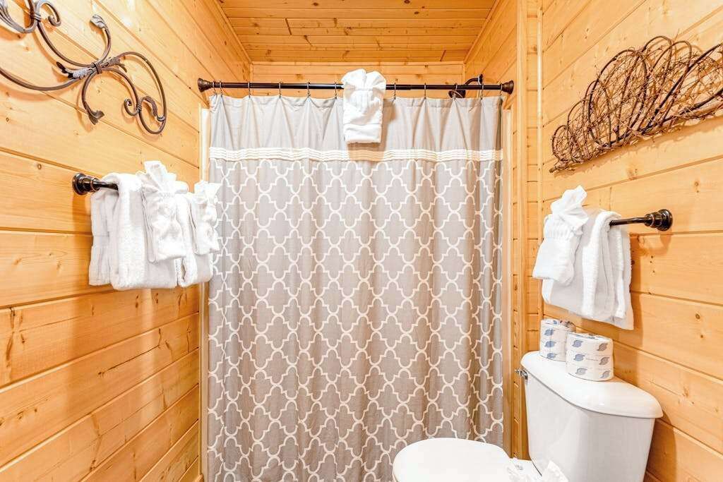 A wooden cabin bathroom with a shower curtain, toilet, and towels hanging on the wall.
