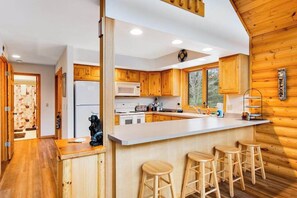 A modern kitchen with wooden cabinets, a white countertop, and a bar area with stools. - Secluded, dog-friendly home with tree-lined view, firepit, fireplace, & deck (Friendship)