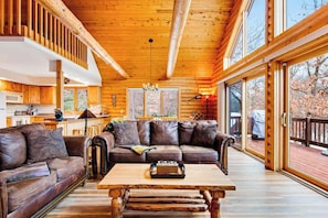 A log cabin interior with a wooden ceiling, a sofa, a coffee table, and large windows. - Secluded, dog-friendly home with tree-lined view, firepit, fireplace, & deck (Friendship)