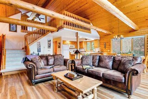 A log cabin interior with a wooden staircase, leather sofas, a dining table, and a kitchen area. - Secluded, dog-friendly home with tree-lined view, firepit, fireplace, & deck (Friendship)