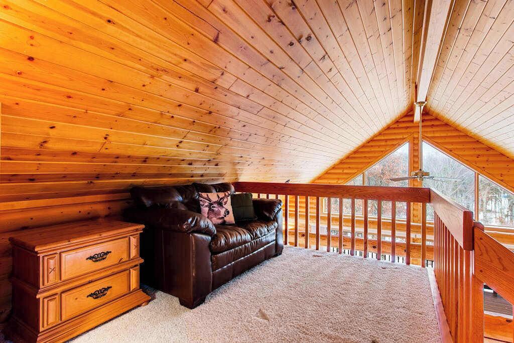 Un interior de madera con techo inclinado, un sofá de cuero y un cojín con forma de ciervo, junto a un aparador de madera.