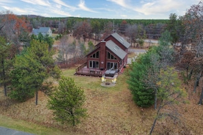 A two-story cabin with a deck, surrounded by trees and a clear sky. - Charming Golf View Home, w/ Hot tub, Sauna, Fire pit, near Lakes & Trails! (Nekoosa)