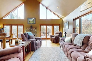 A spacious living room with a high ceiling, large windows, and a fireplace. - Charming Golf View Home, w/ Hot tub, Sauna, Fire pit, near Lakes & Trails! (Nekoosa)