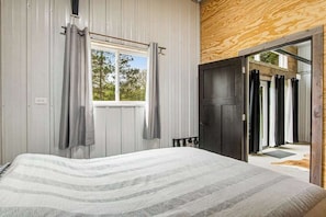 Ein Schlafzimmer mit Bett, Vorhängen, einem Fenster und einer Tür zu einem Außenbereich.