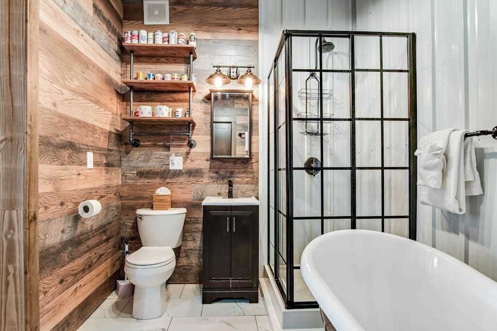Une salle de bain avec un mur en bois, des toilettes blanches, un meuble sombre, une cabine de douche en verre et une baignoire blanche.