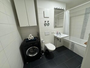 Une salle de bain équipée d’un lave-linge, de toilettes, d’un lavabo et d’une douche.
