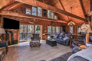 A log cabin interior with a fireplace, leather furniture, and large windows.