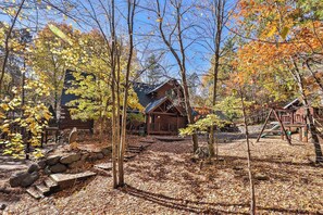 A cabin surrounded by trees with autumn leaves, a wooden deck, and a stone wall.