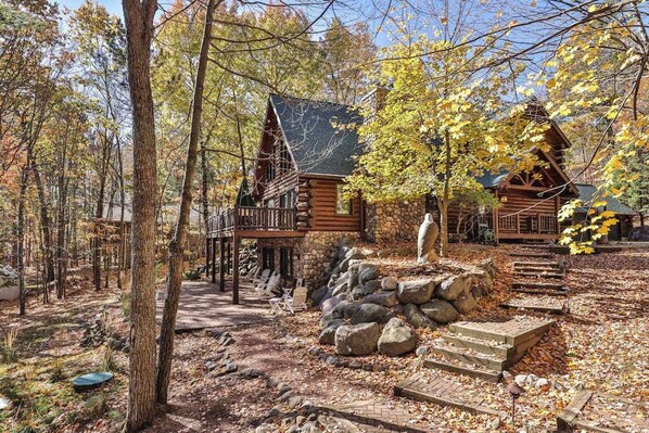 A log cabin with a balcony, surrounded by trees and a stone pathway.