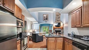 A modern kitchen with wooden cabinets, stainless steel appliances, and a stone fireplace. - Cozy Fireside Condo with Jetted Tub & AC (Wisconsin Dells)