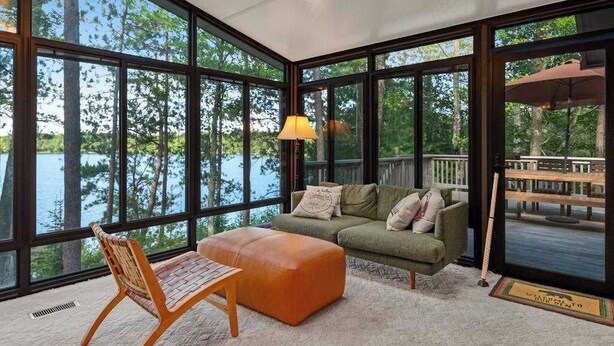 A room with large windows, a sofa, an ottoman, and a chair. - Lakefront home w/ deck, grill, fireplace, firepit, AC, & WiFi (Eagle River)