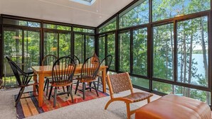 A sunroom with a dining table and chairs, large windows, and a ceiling fan. - Lakefront home w/ deck, grill, fireplace, firepit, AC, & WiFi (Eagle River)