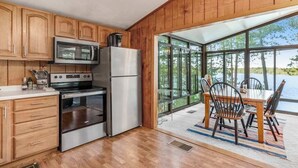 A modern kitchen with wooden cabinets, stainless steel appliances, and a large window overlooking a body of water. - Lakefront home w/ deck, grill, fireplace, firepit, AC, & WiFi (Eagle River)
