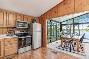 A modern kitchen with wooden cabinets, stainless steel appliances, and a large window overlooking a body of water. - Lakefront home w/ deck, grill, fireplace, firepit, AC, & WiFi (Eagle River)