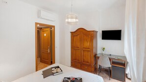 Une chambre à coucher comprenant un lit, une table de chevet, une armoire en bois, un bureau, une chaise et un téléviseur.