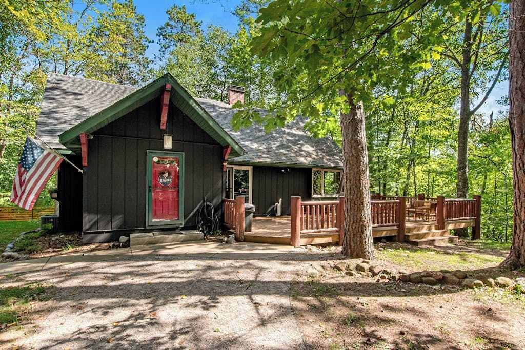 A rustic cabin with a wooden deck, a red door, and an American flag.
