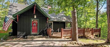 A rustic cabin with a wooden deck, a red door, and an American flag.