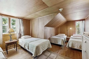 Una habitación con tres camas, paredes de madera y techo inclinado.