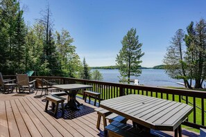 A wooden deck with tables and chairs overlooking a lake. - Lakefront lodge with private dock, firepit, deck & sunset views (Eagle River)