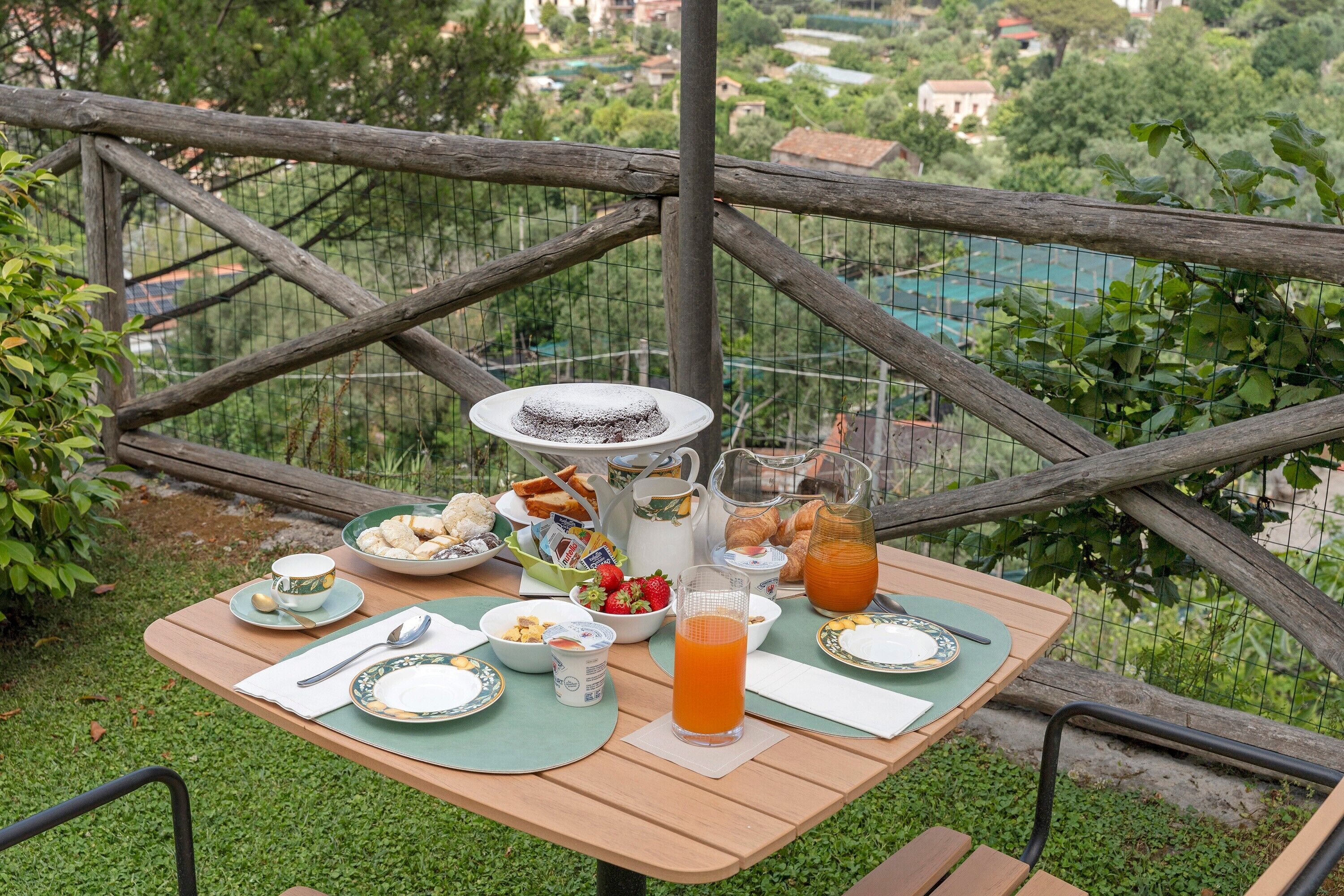 Una mesa de picnic con platos, vasos y una jarra de jugo, rodeada de follaje y una cerca.