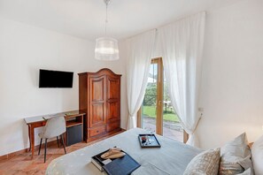 Ein Schlafzimmer mit Bett, Schreibtisch, Stuhl, Fernseher und einem Fenster mit Vorhängen.