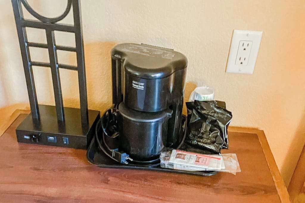 A coffee maker on a wooden table with a power strip and a bag of coffee pods.