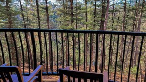 Ein Balkon mit zwei Holzstühlen und einem kleinen Tisch, mit Blick auf einen bewaldeten Bereich.