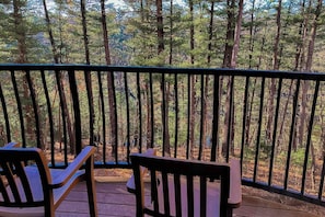 Ein Balkon mit zwei Holzstühlen und einem kleinen Tisch, mit Blick auf einen bewaldeten Bereich.