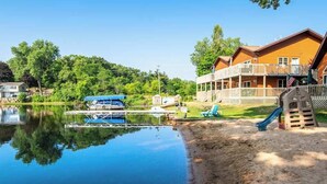 A lakeside property with a dock, boats, a playground, and a large wooden building with a balcony.