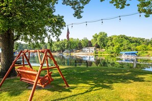 A swing set, an American flag, a bench, a dock, and a house by a lake.