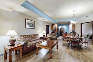 Ein Wohnzimmer mit Sofa, Couchtisch und Esstisch mit Stühlen. Im Hintergrund ist eine Küchenzeile zu sehen.
