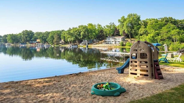 Un parc au bord du lac, avec une aire de jeux, un quai pour bateaux et des maisons en arrière-plan.