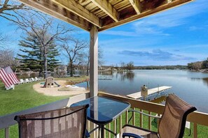 A lakeside patio with a table and chairs, a small play area, and a dock extending into the water. - Inviting lakefront condo - amazing views, beach access, fireplace, dock, AC, W/D (Wisconsin Dells)