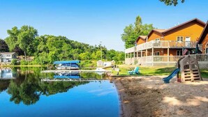 Un chalet au bord du lac, avec un quai, un bateau et une aire de jeux.