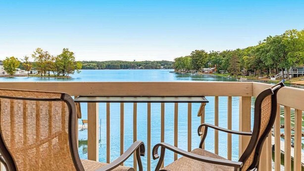Ein Balkon mit Korbstühlen mit Blick auf einen See, umgeben von Bäumen und Gebäuden.
