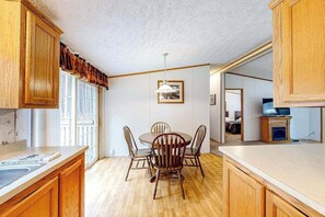 A kitchen with wooden cabinets, a dining table with chairs, a hanging light fixture, and a television on a stand.