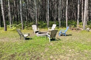 A forested area with outdoor seating including chairs and a fire pit.
