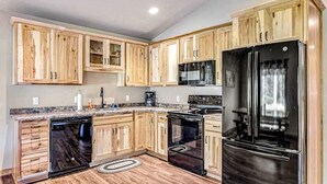 A kitchen with wooden cabinets, a black refrigerator, a microwave, and a dishwasher. - Dog-friendly cabin with hot tub, fireplace, patio, grill, central AC, & W/D (Conover)